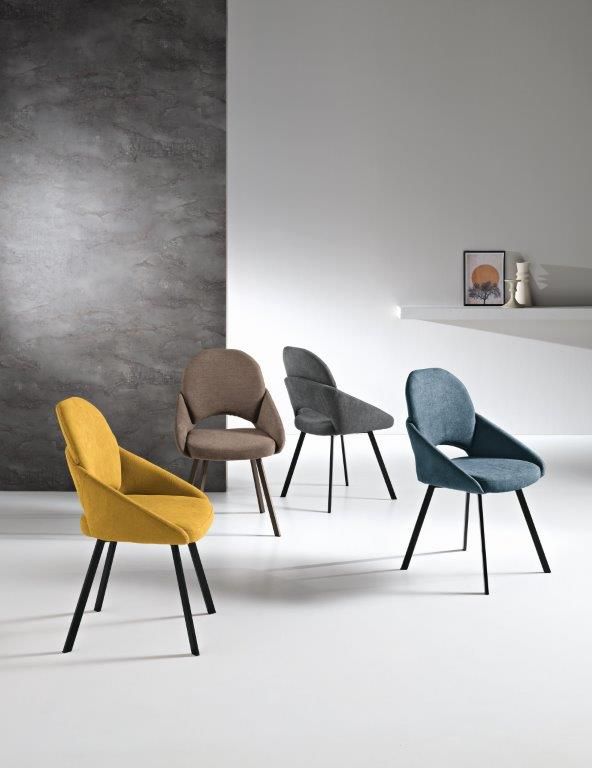 Quattro sedie moderne di diversi colori, con gambe nere, contro una parete strutturata.