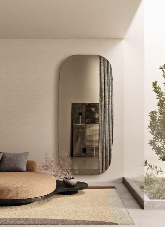 Un grande specchio ovale riflette un'opera d'arte astratta e uno spazio abitativo dai toni neutri.
