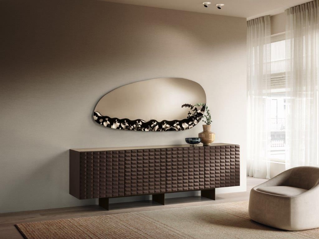 Mobiletto trapuntato marrone con specchio decorativo, vaso e sedia in una stanza dai toni neutri.