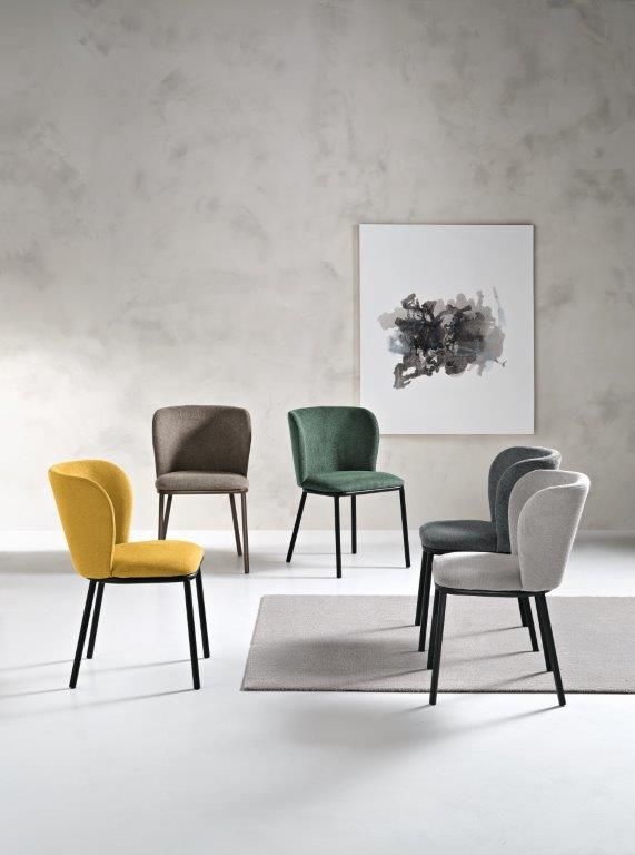 Sedie da pranzo di vari colori contro una parete neutra; è visibile un'opera d'arte astratta incorniciata.