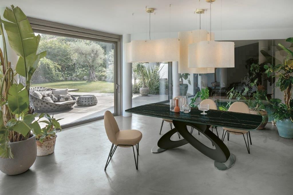 Sala da pranzo con tavolo verde, sedie beige, grande finestra con vista sul giardino e lampadario.