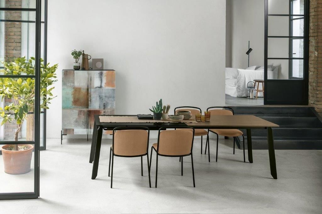 Sala da pranzo con tavolo, sedie, mobiletto colorato e ampie finestre.