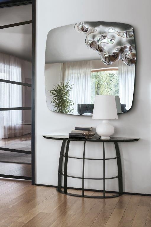 Ingresso moderno con specchio dai bordi ondulati sopra la consolle con lampada e decorazioni.