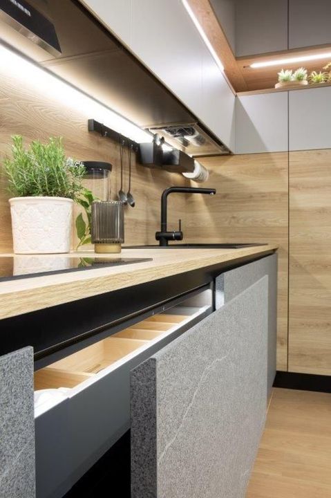 Cucina moderna con cassetto aperto, ripiani in legno, mobili grigi e rubinetto nero.