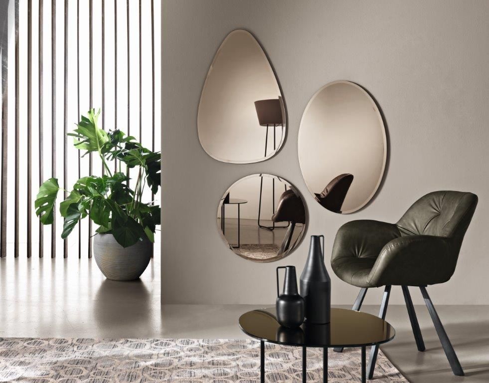 Tre specchi color bronzo su una parete, una pianta e una sedia verde in un ambiente interno moderno.