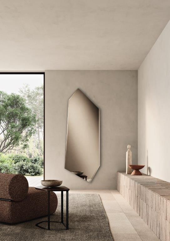 Un soggiorno moderno con un grande specchio dalla forma irregolare, un divano marrone e scaffali in legno.