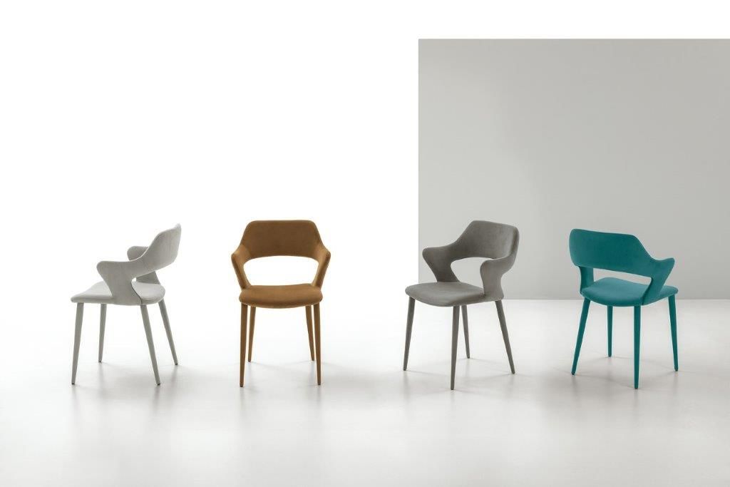 Quattro poltrone moderne nei colori grigio, marrone chiaro, grigio e verde acqua su sfondo bianco.