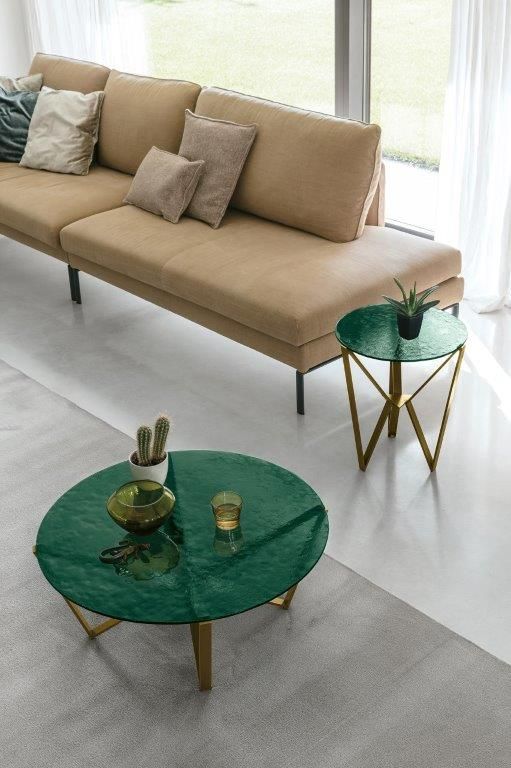 Divano beige con cuscini, tavolino da caffè in vetro verde, tavolino laterale e piante da interno.