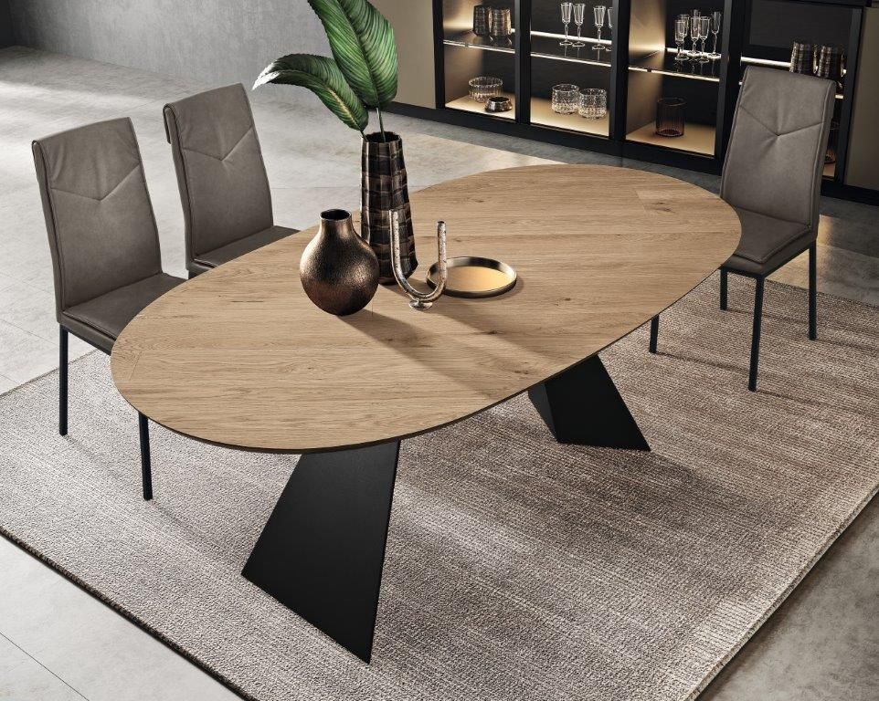 Tavolo da pranzo ovale in legno con gambe nere, circondato da sedie grigie su un tappeto.