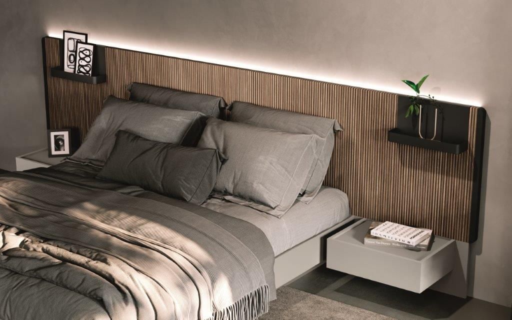 Camera da letto con testiera in legno, comodini sospesi e biancheria grigia con cuscini decorativi.