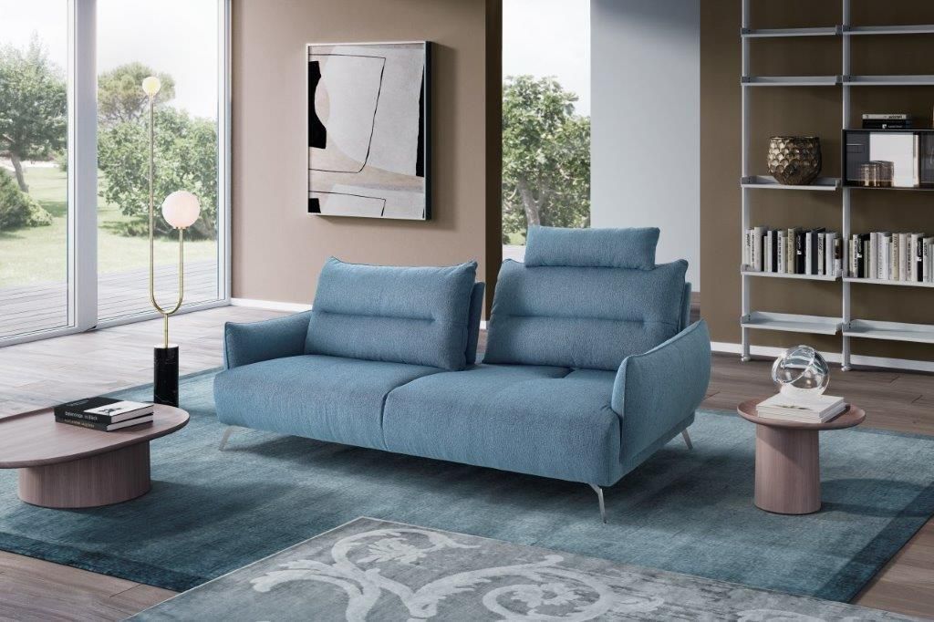 Divano blu in un soggiorno moderno con un grande tappeto, tavolini laterali e una lampada da terra.