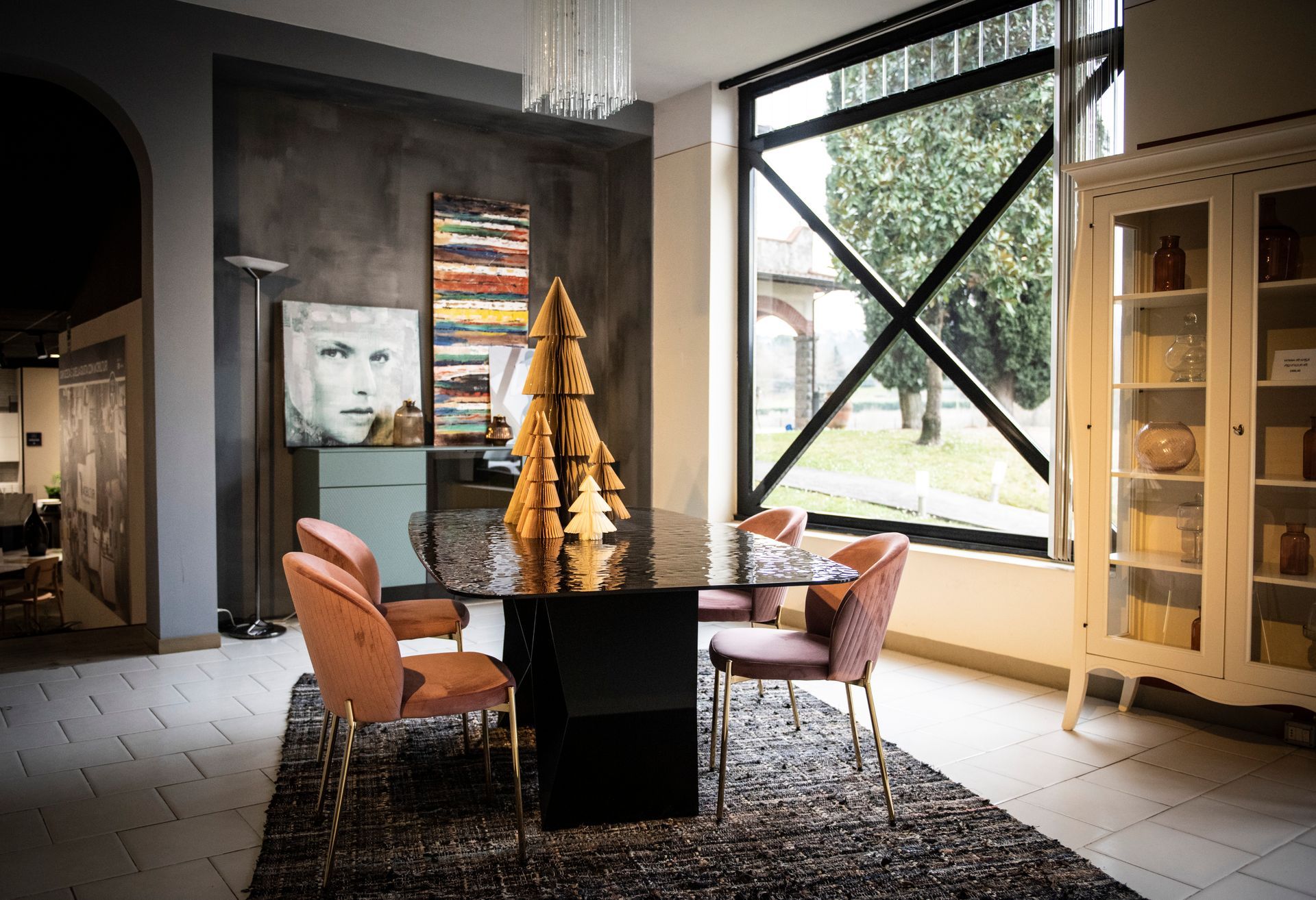 Sala da pranzo con tavolo nero, sedie in velluto rosa, grande finestra e credenza.