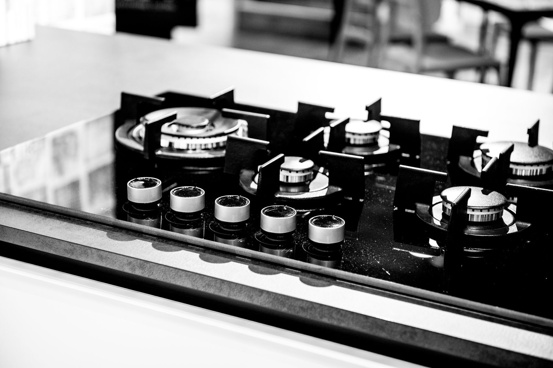 Primo piano in bianco e nero di un moderno piano cottura a gas con cinque fuochi e manopole di controllo.