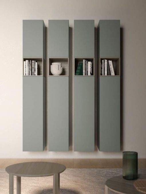 Quattro contenitori verticali a parete, di un colore verde tenue, con nicchie aperte contenenti libri e un vaso.