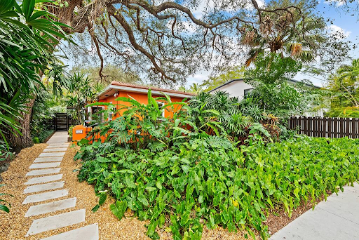 A small orange house is surrounded by lots of green plants and trees.