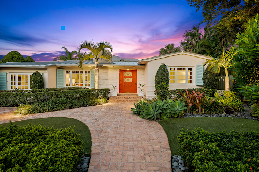 The front of a house with a brick driveway and a sunset in the background.