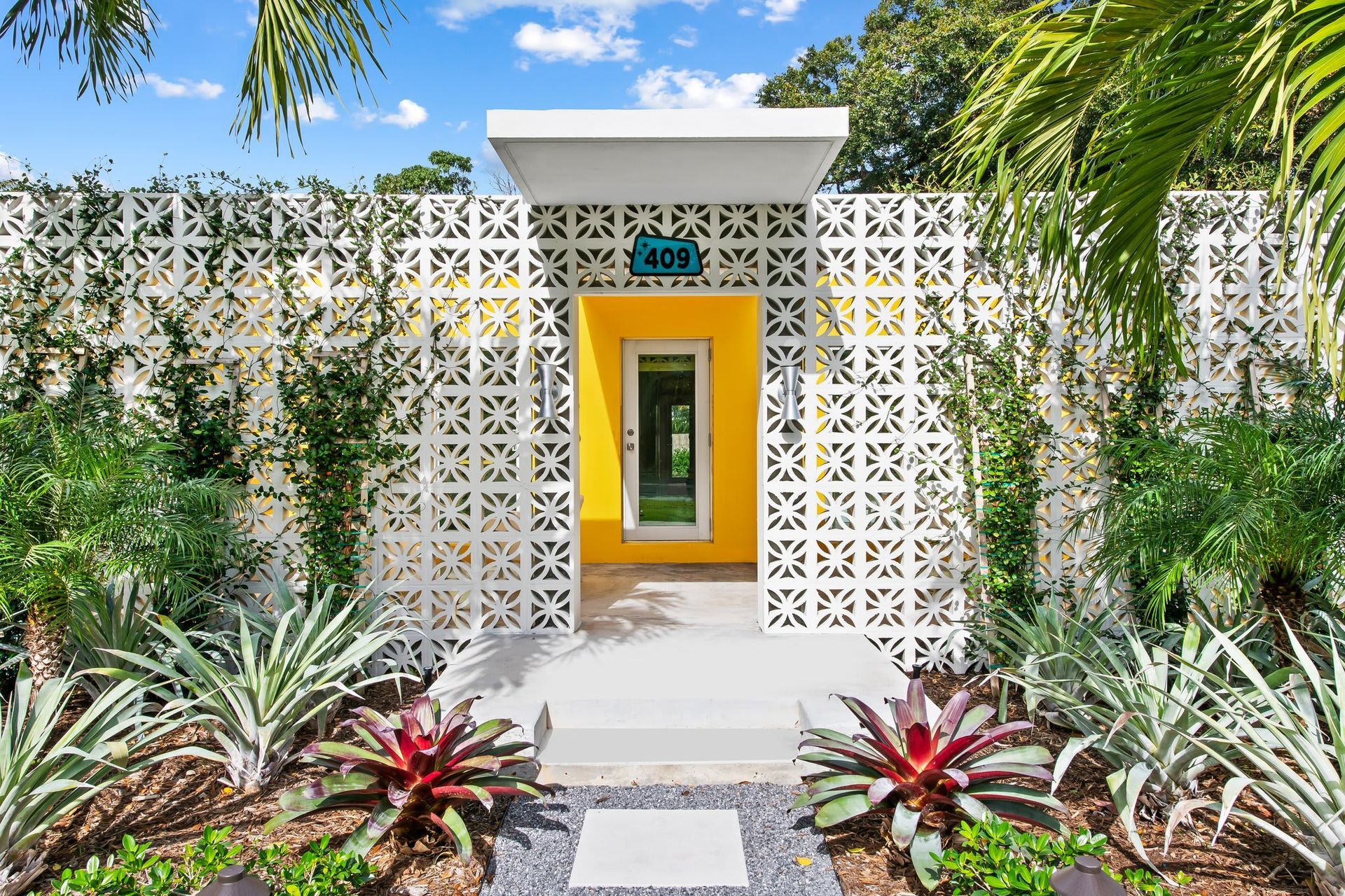 A small orange house is surrounded by lots of green plants and trees.