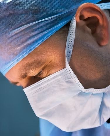 Surgeon in blue surgical cap and mask, looking down intently.
