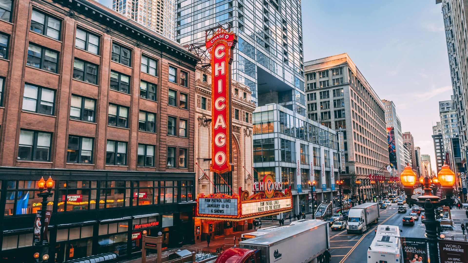 Chicago Theatre marquee lit up amidst busy downtown street, many cars, and skyscrapers.