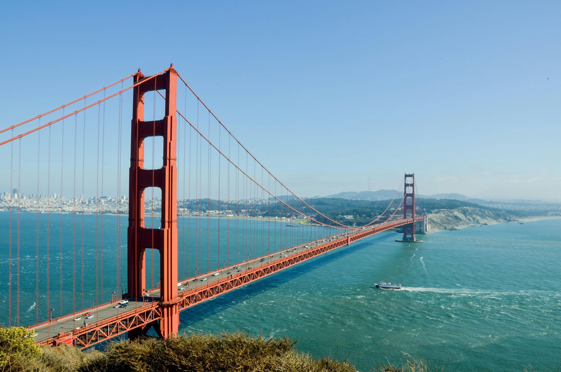 Golden Gate Bridge, red structure spanning turquoise water on a clear, sunny day; San Francisco in the background.