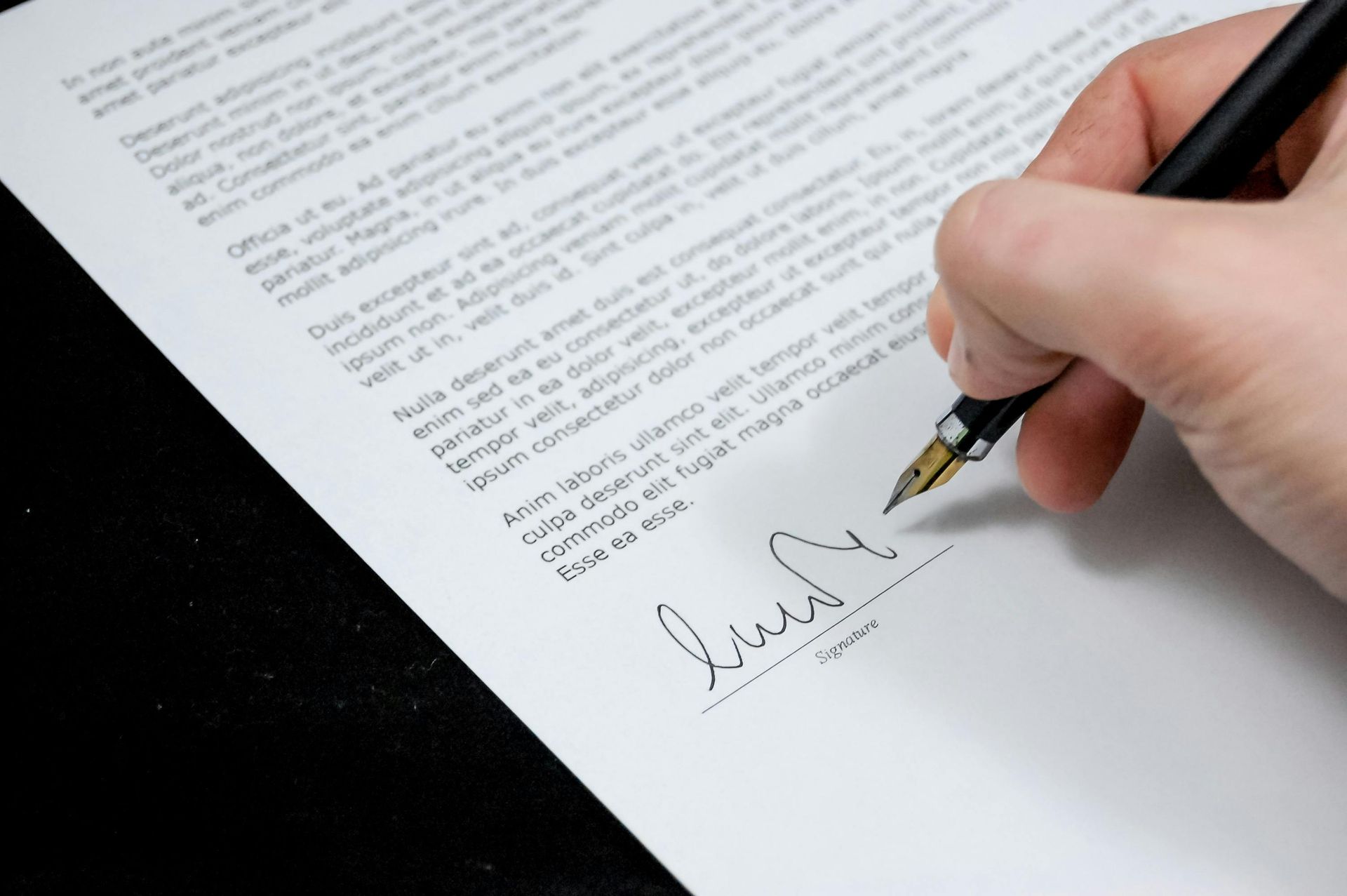 A hand signing a document with a fountain pen on a white paper; close-up.