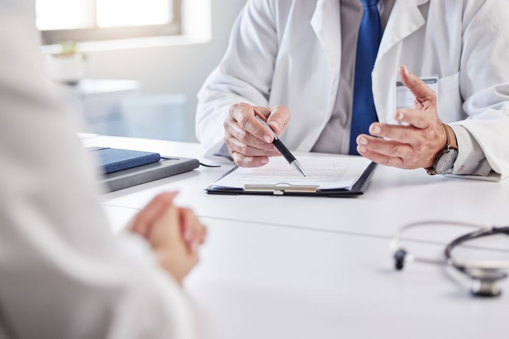 Doctor in white coat reviews paperwork with patient, stethoscope on desk.