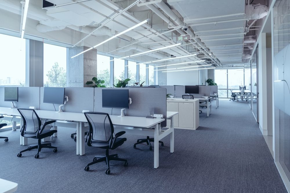 Modern office with desks, chairs, computers, and gray cubicle dividers.  Natural light floods the space.
