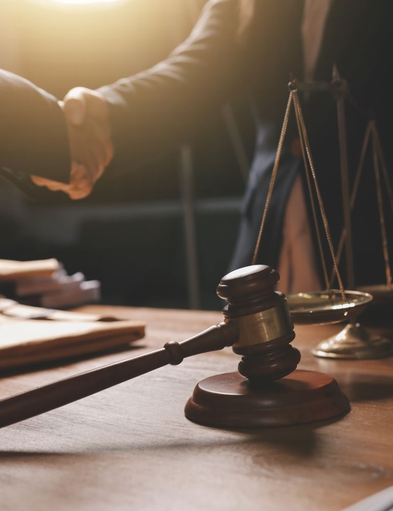 Gavel, scales of justice, and a handshake on a wooden table, symbolizing a legal agreement.