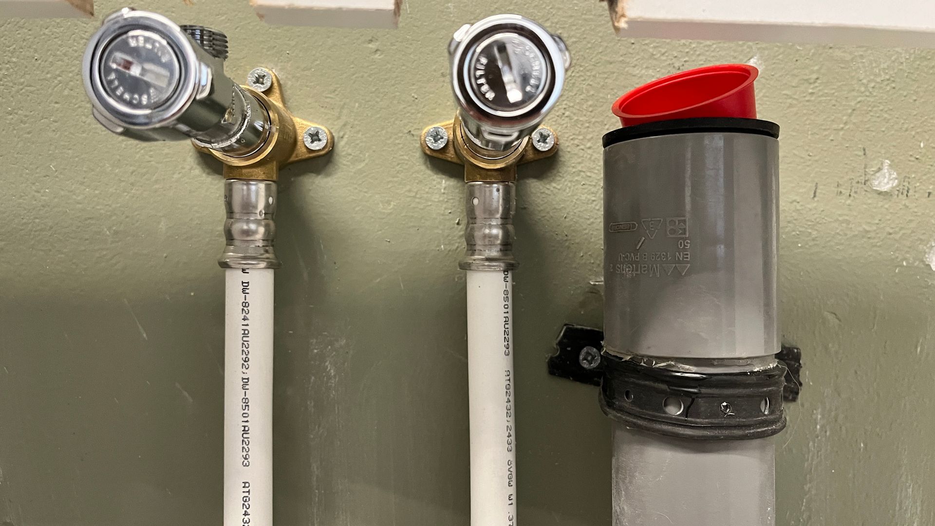 Een close-up van drie pijpen en kleppen op een muur.