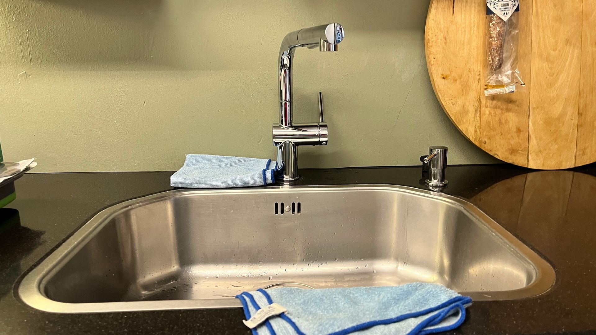 Een roestvrijstalen keukenspoelbak met een houten snijplank op de achtergrond.