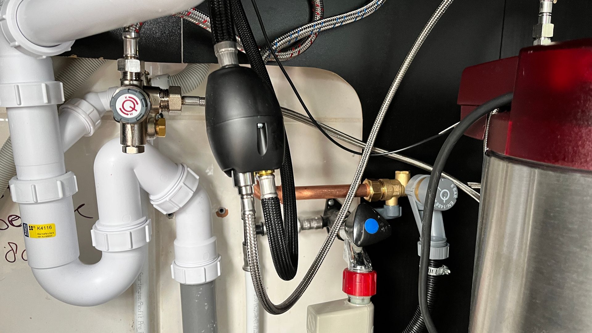 Een close-up van een gootsteen met veel leidingen en draden