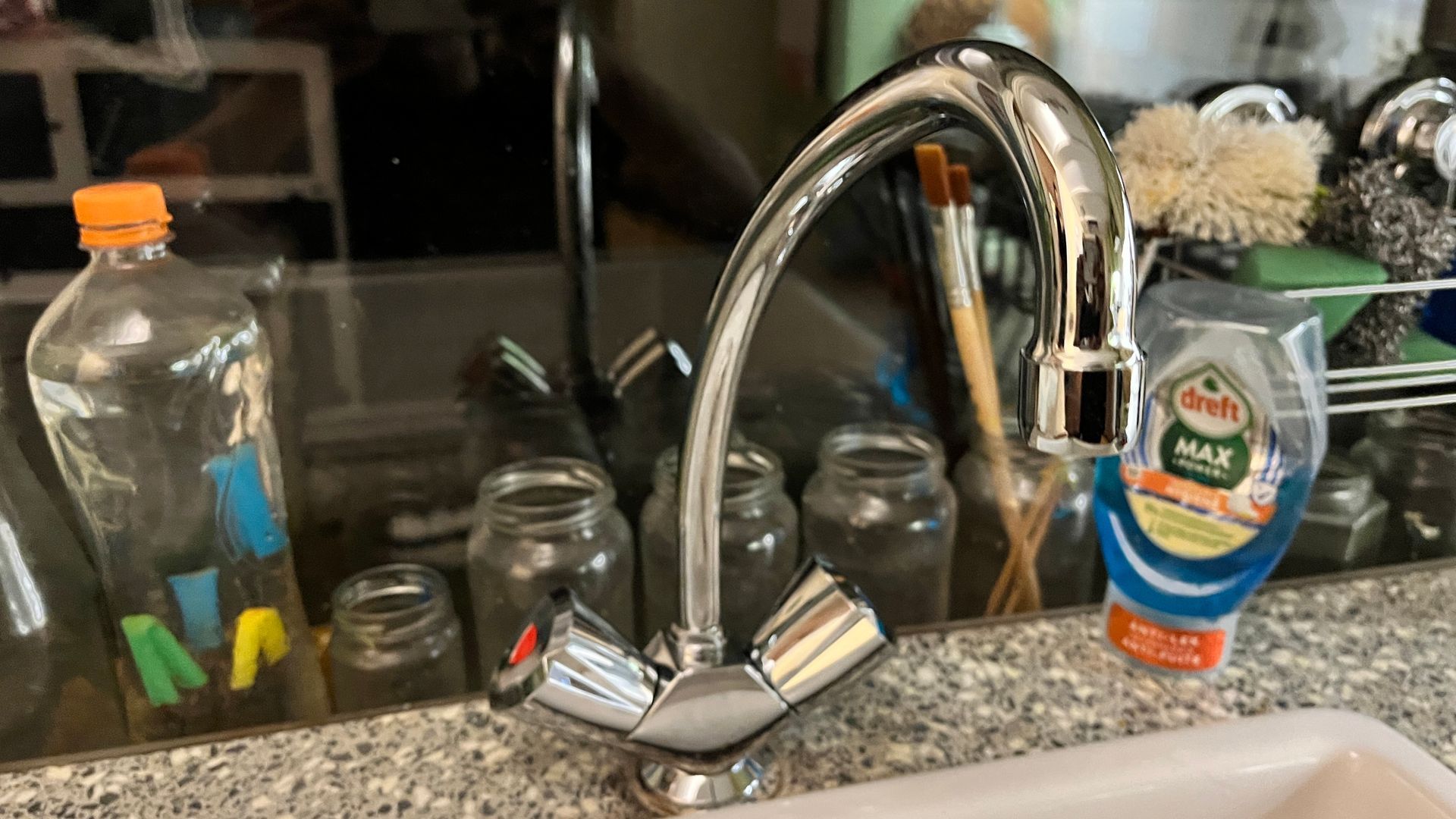 Een gootsteen met een kraan en een fles afwasmiddel op het aanrecht.