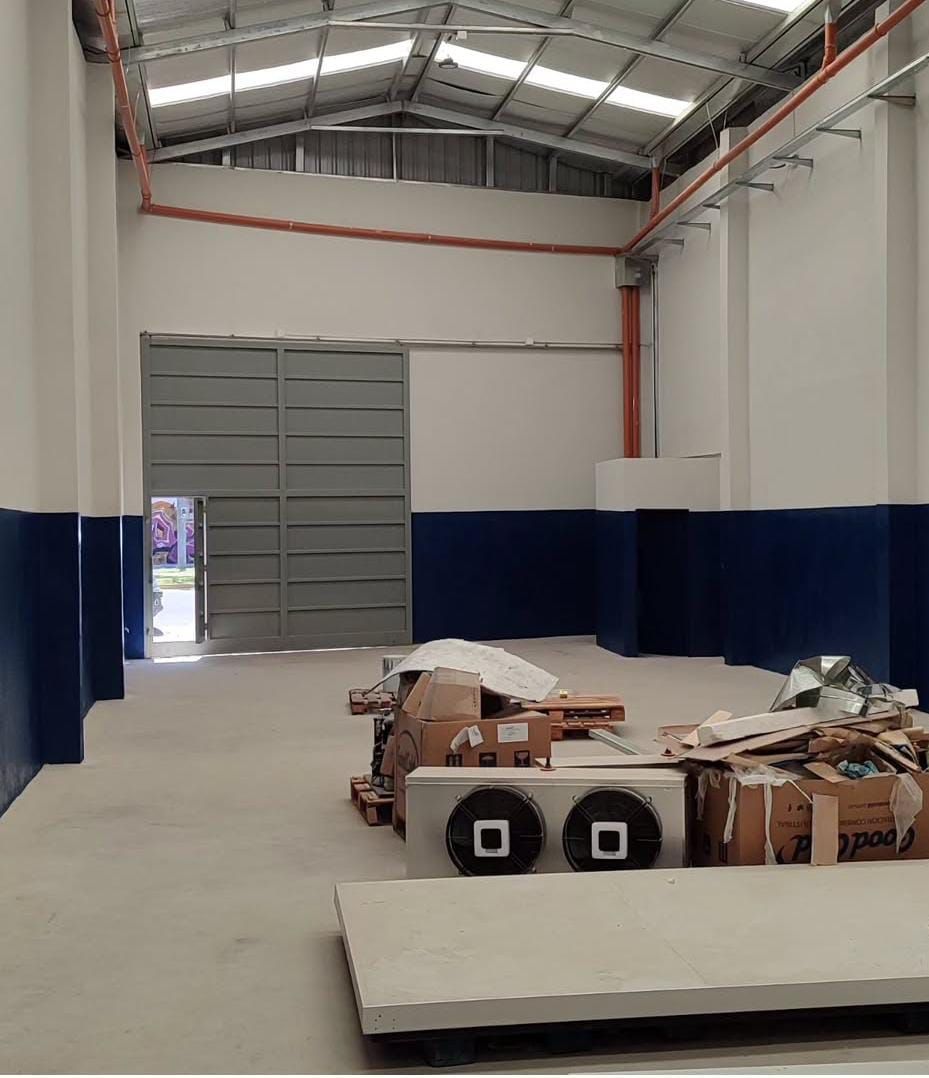 Interior vacío de un almacén con puerta metálica gris abierta, paredes azules y blancas y escombros en el suelo.