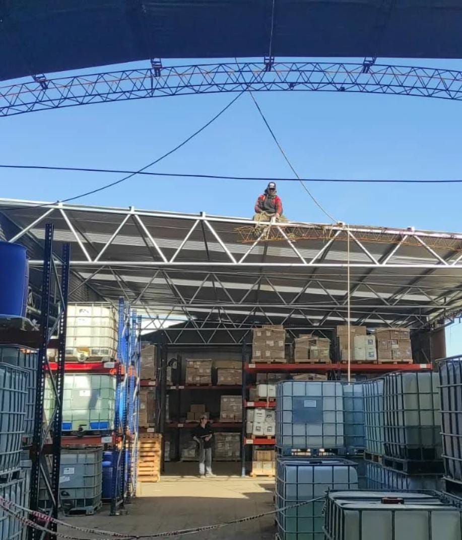 Persona trabajando en una estructura sobre el techo metálico de un almacén, bajo un cielo azul. Debajo se encuentran los tanques de almacenamiento.