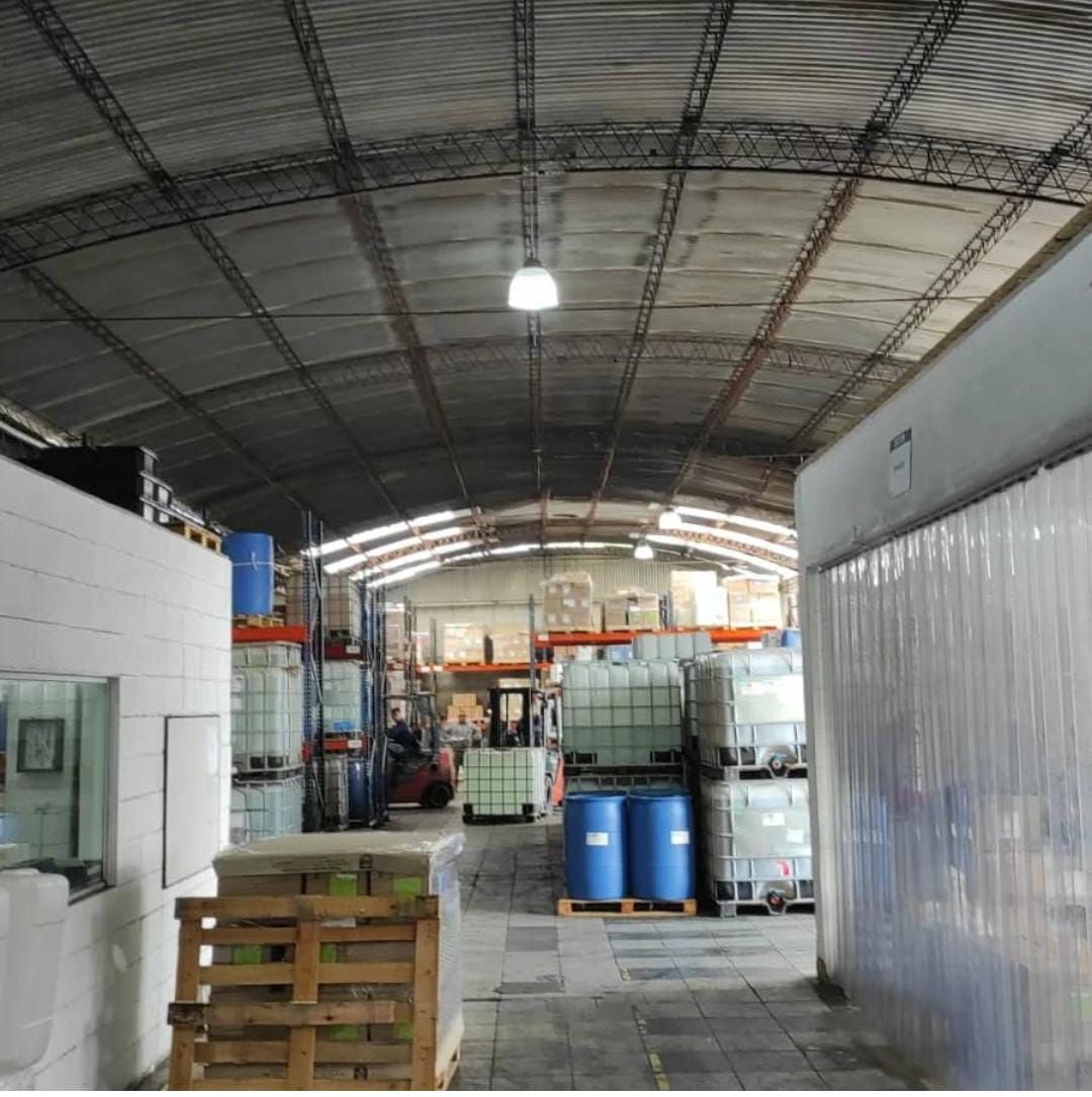 Interior de almacén con contenedores y palets apilados. Se ve una carretilla elevadora.