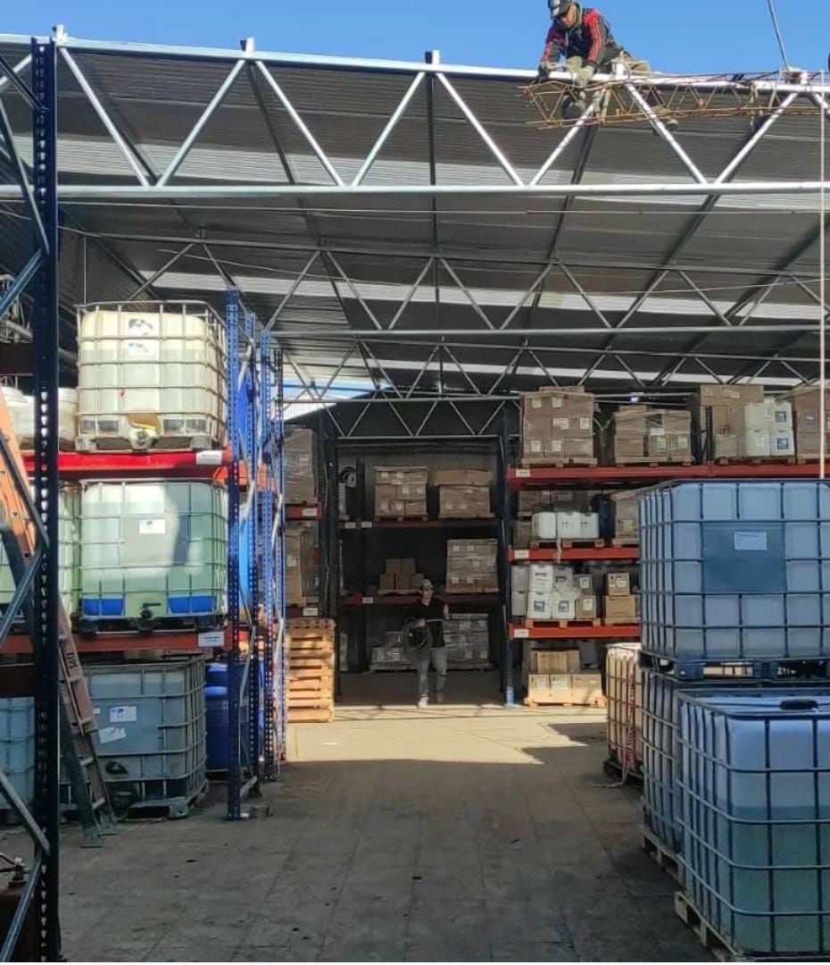 Interior de almacén con estanterías, estructura del techo y trabajador en el tejado.