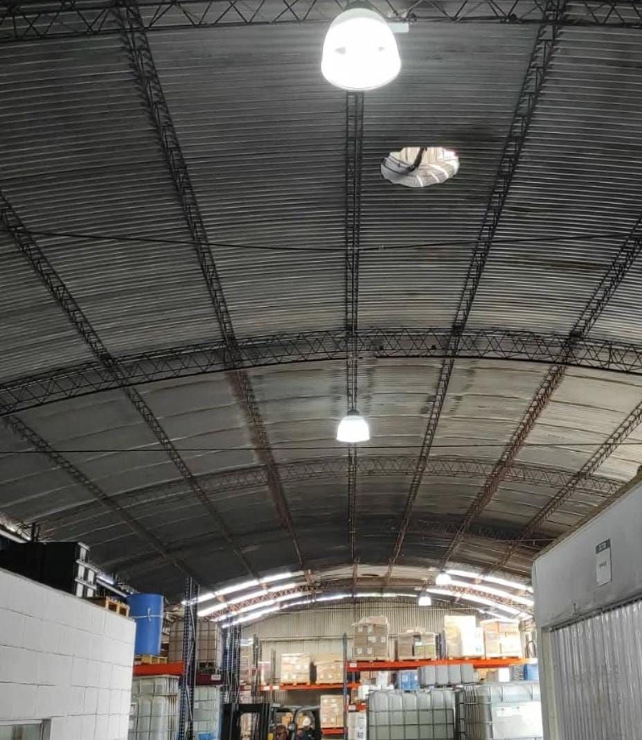Interior de un almacén con techo metálico arqueado, luces brillantes y suministros a la vista.