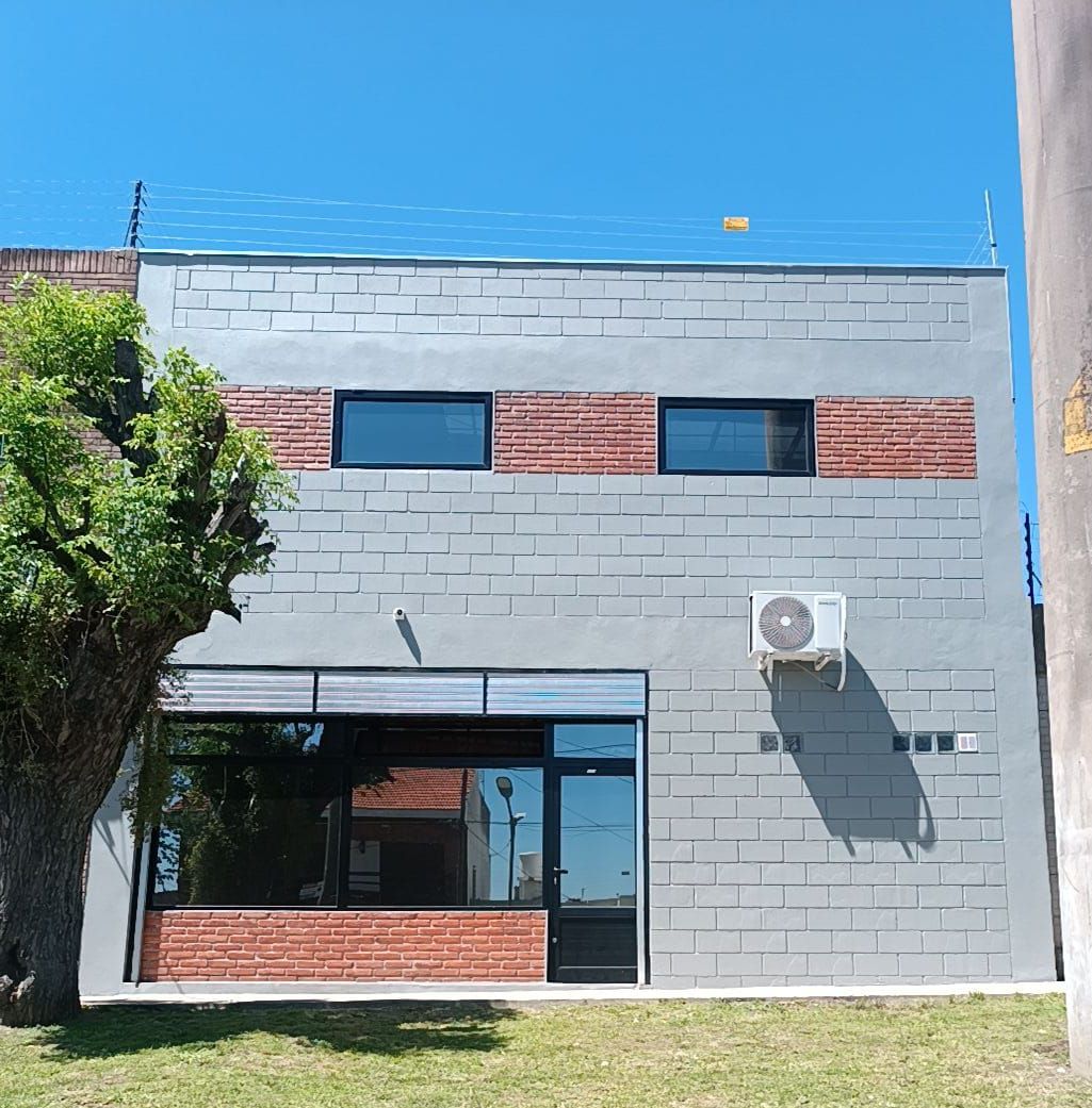 Edificio de ladrillo gris con detalles, ventanas y unidad de aire acondicionado de ladrillo rojo. Cielo azul despejado.