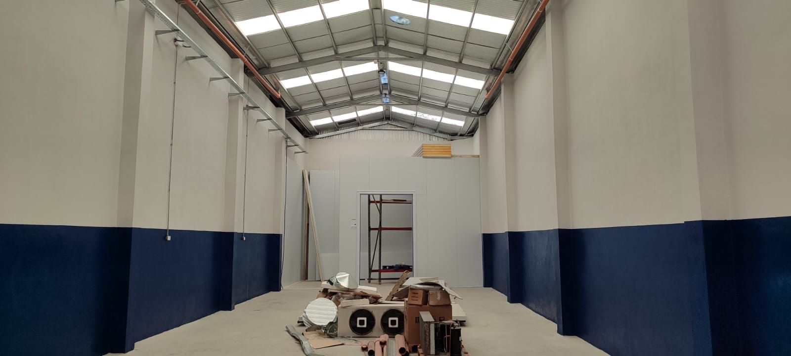 Interior de un gran almacén vacío con techos altos, paredes blancas y base azul.