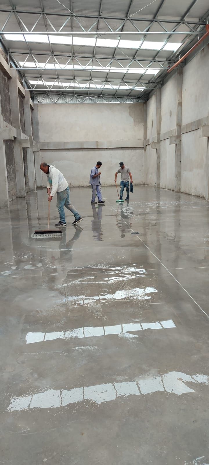 Tres trabajadores alisando un suelo de hormigón brillante y húmedo en un gran almacén vacío.