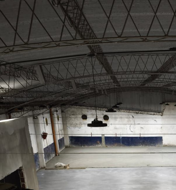 Vista interior de un gran edificio industrial vacío con techo de vigas metálicas y suelo de hormigón.