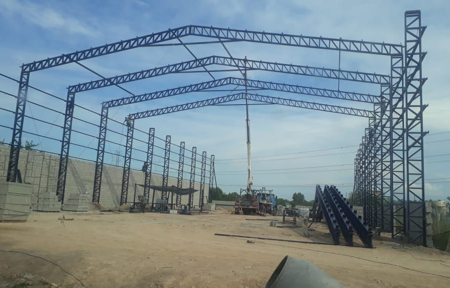 Estructura de acero de un almacén en construcción, con una grúa en el centro, al aire libre.