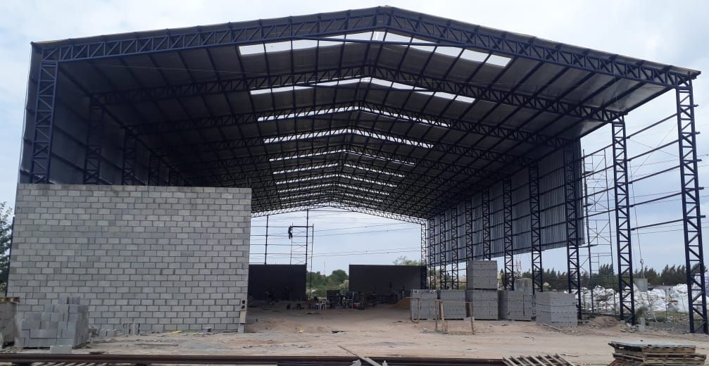 Gran almacén metálico con paredes y techo grises bajo un cielo nublado.