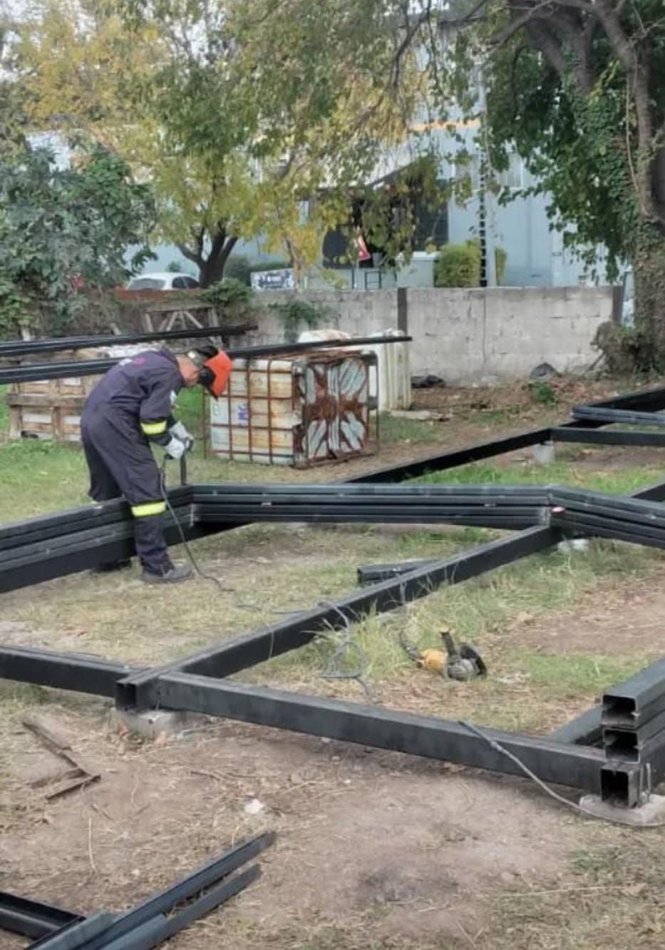 Persona con traje de trabajo soldando una estructura metálica al aire libre.