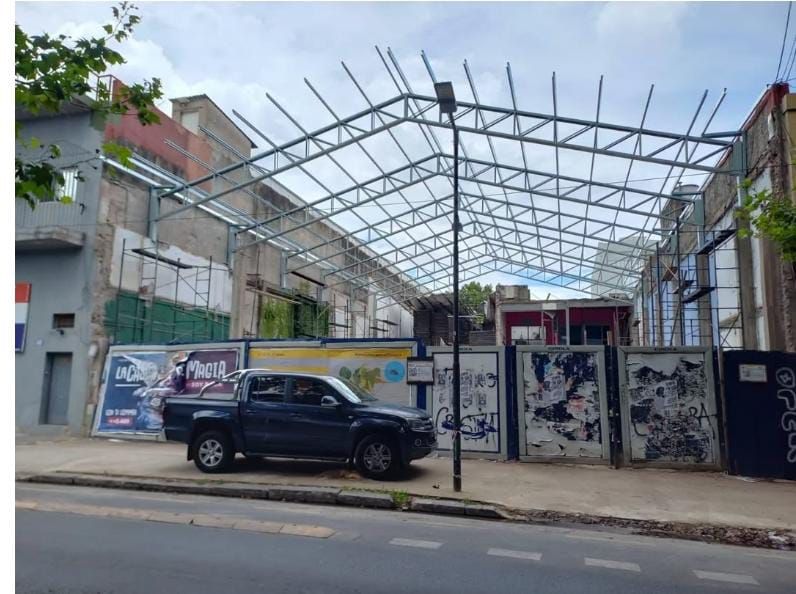 Estructura metálica en construcción sobre un edificio. Una camioneta oscura está estacionada en la calle.