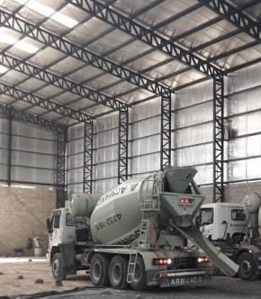 Dos camiones hormigonera vertiendo hormigón sobre un suelo reforzado con barras de acero dentro de un almacén.