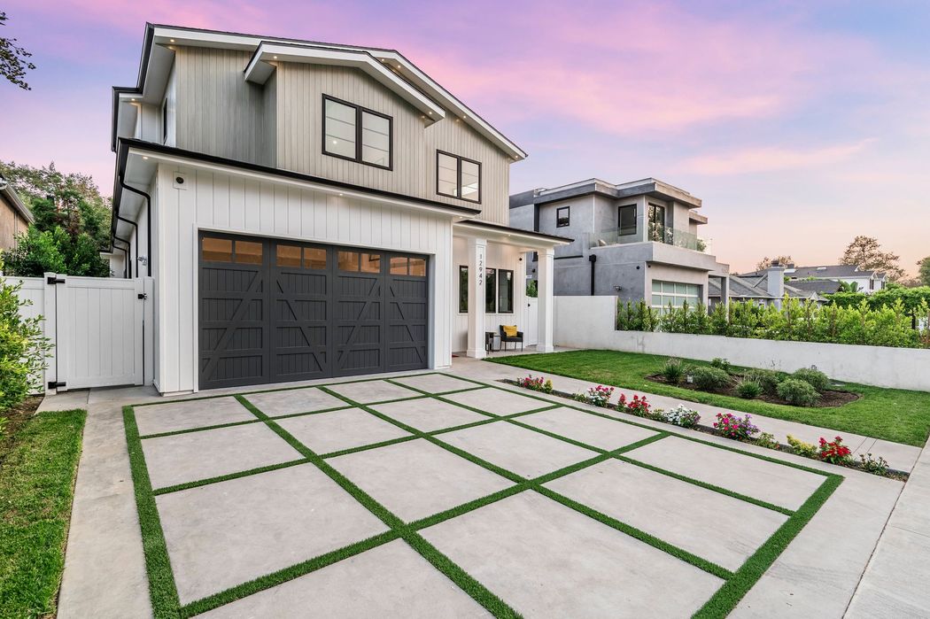 A large white house with a black garage door and a concrete driveway.
