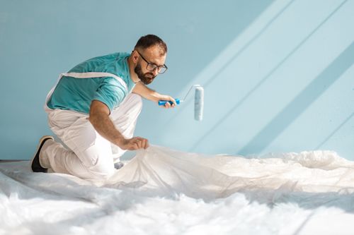 Engaged home painter adjusting floor sheet for painting.