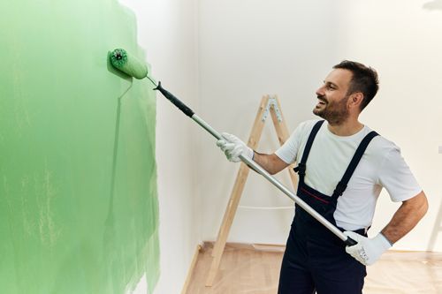 Happy male house painter painting the wall in green. Happy male house painter painting the wall in green.