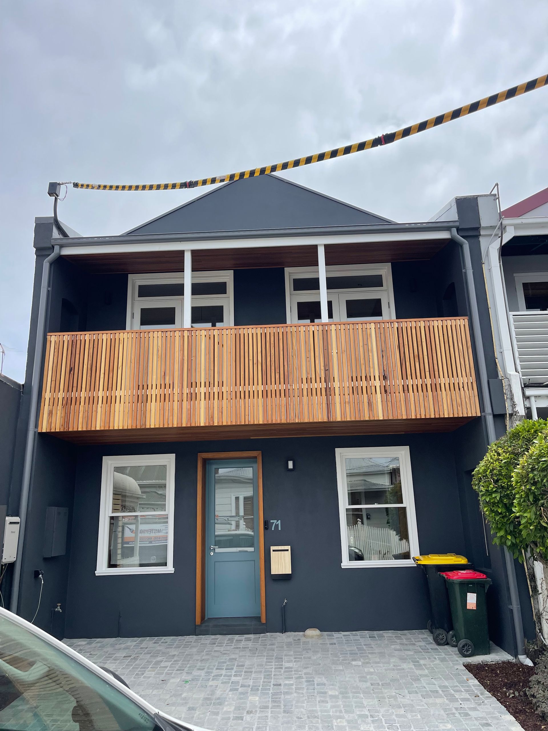 A black house with a wooden balcony and a car parked in front of it.